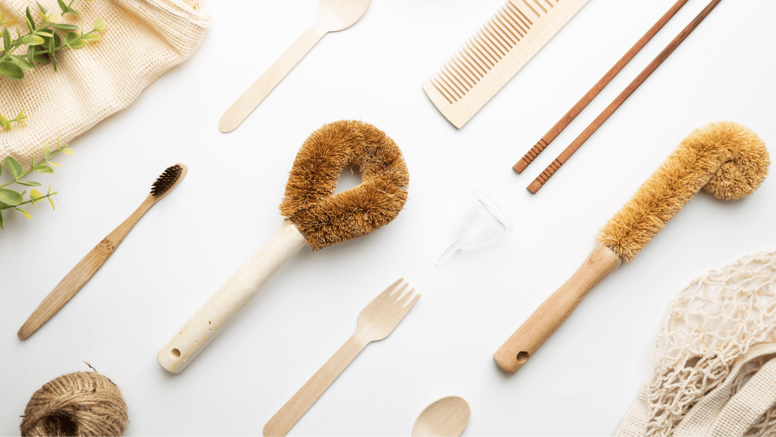 A flat lay of eco-friendly, plastic-free household items including bamboo toothbrushes, wooden combs, cutlery, a menstrual cup, and a natural fibre brush. The items are arranged neatly on a white background, emphasising sustainability and zero-waste living
