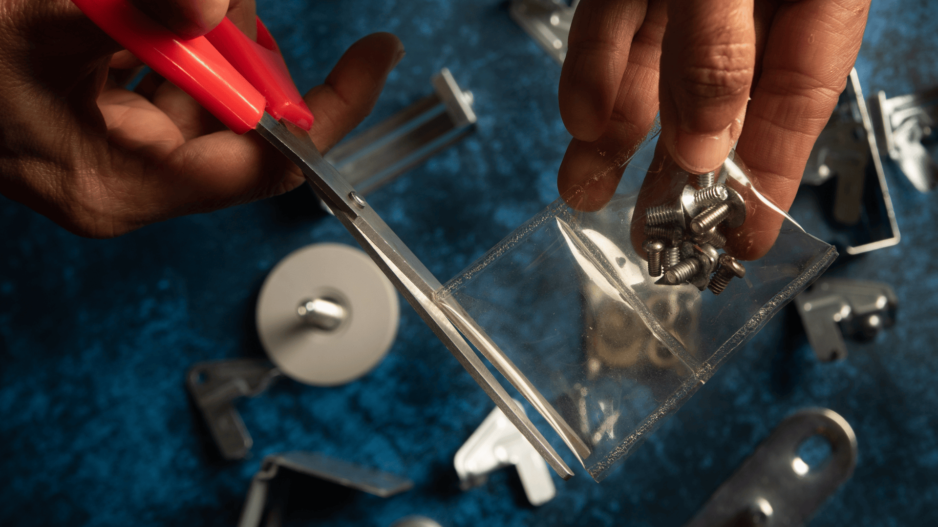 Hand cutting a transparent, biodegradable seaweed-based pouch holding metal screws, showcasing innovative packaging by Zerocircle, a startup supported by Scale-Up, the no-equity accelerator by Marico Innovation Foundation.