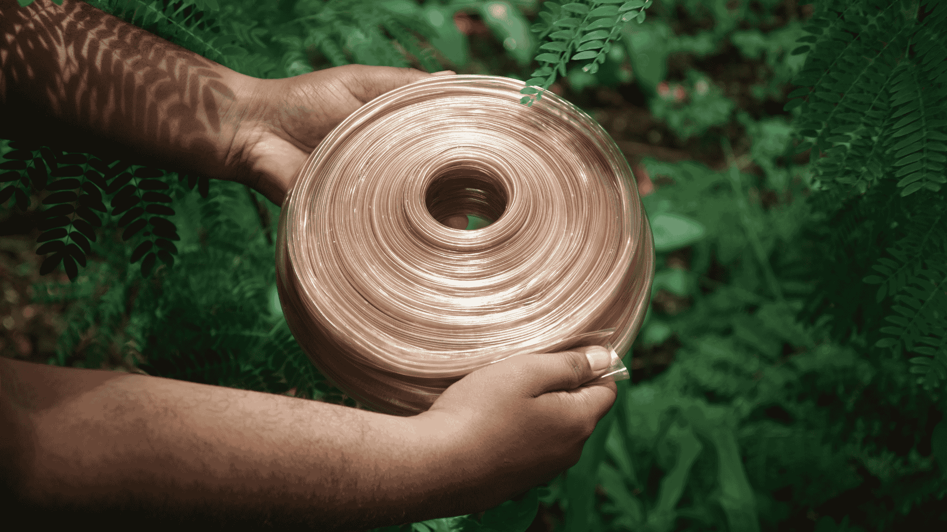 Hands holding a large roll of transparent, biodegradable packaging film outdoors.