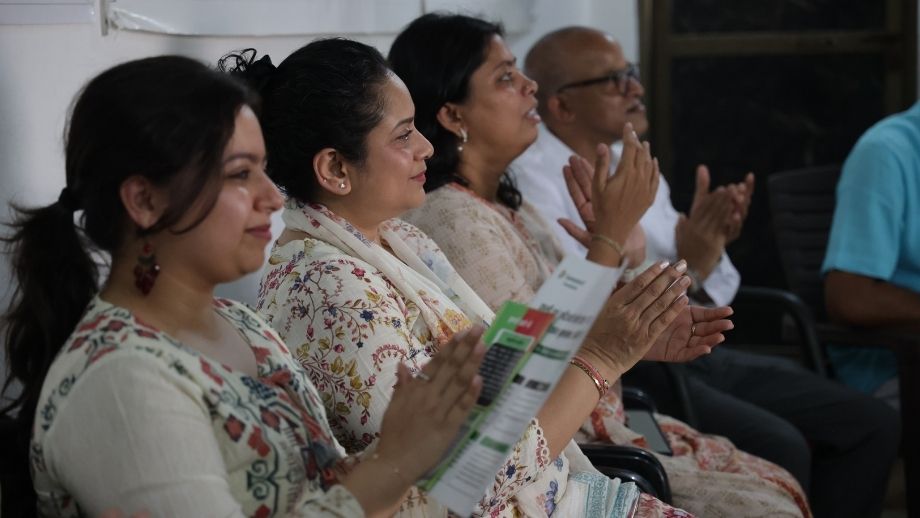 Team MIF in the foreground holding pamphlets, smiling and clapping during a presentation.