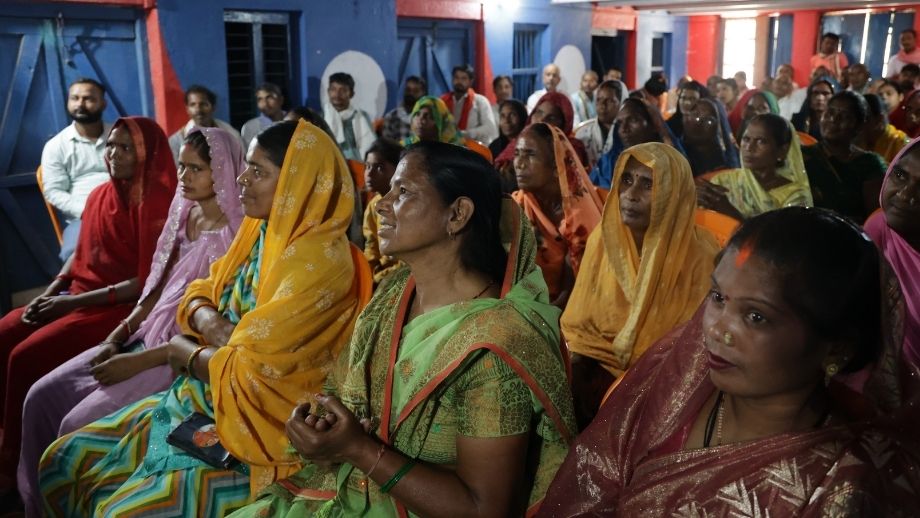 Women farmers in bright saris listening closely during a community tech-pilot gathering.
